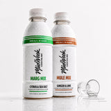 Two Midweek Cocktail Mix bottles, one Citrus & Sea Salt (Marg Mix) with a green band and one Ginger & Lime (Mule Mix) with an orange band, both covered in condensation, with an empty shot glass on a white reflective surface.